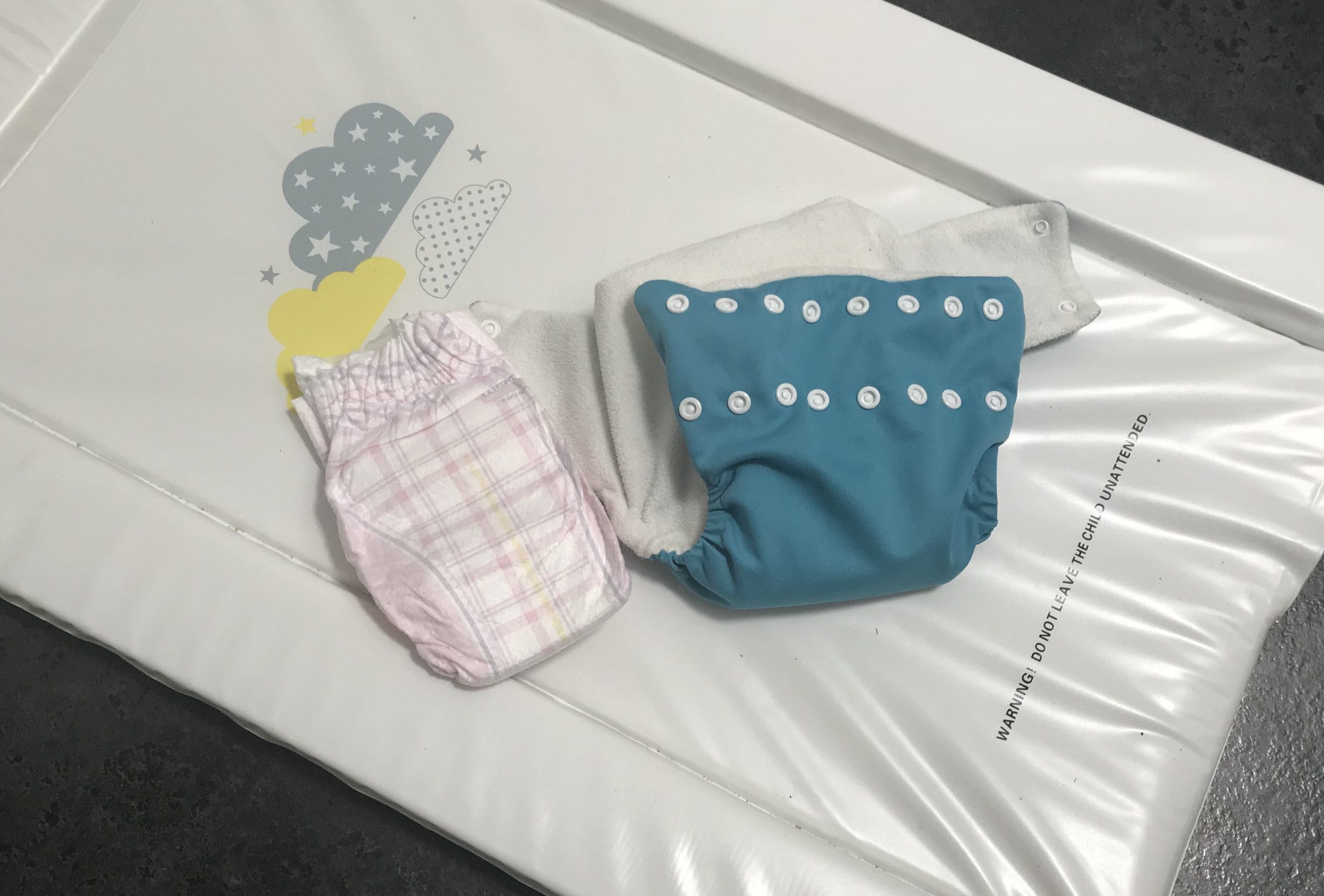 A reusable modern cloth nappy and a disposable nappy on a change mat